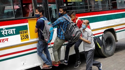 Migrant workers hang on to a door of a moving bus as they return to their villages after Delhi government ordered a six-day lockdown. Reuters
