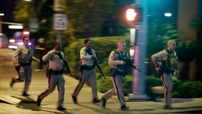 Police run to cover at the scene of a shooting near the Mandalay Bay resort and casino on the Las Vegas Strip, Sunday, Oct. 1, 2017, in Las Vegas. Multiple victims were being transported to hospitals after a shooting late Sunday at a music festival on the Las Vegas Strip. (AP Photo/John Locher)