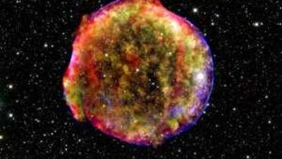 The blazing cloud of expanding debris is green and yellow, while the blast's shockwave is blue, in this image of the Tycho supernova in the constellation Cassiopeia, about 7,500 light years from Earth.