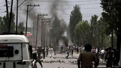 Smoke rises in the background as Kashmiri protesters throw stones at Indian police men during a protest in Srinagar on Monday, June 28, 2010.