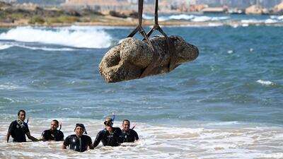 TOPSHOT - Divers watch as a crane pulls a piece of stone from the waters at Abu Qir bay in Alexandria on August 21, 2025, as part of an event organized by the Ministry of Tourism and Antiquities to recover sunken antiquities. (Photo by Khaled DESOUKI / AFP)