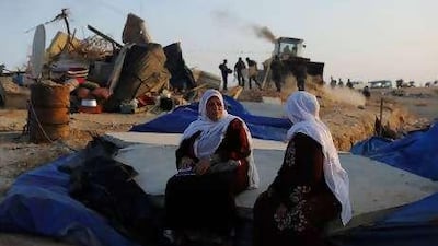Bedouin women sit on rubble as Israeli policemen destroy their makeshift houses in the Negev desert.