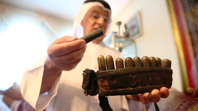Dr Ahmed Khoori with a belt, dating from about the 1830s, and brass containers packed with the correct combination of shot and powder to allow quick reloading of a flintlock rifle. Fatima Al Marzooqi / The National