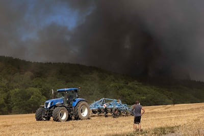 A farmer stands in a field as colleagues arrive with their tractors to help firefighters tackle a nearby forest fire in Thierville, north-west France, on August 12, 2022. In arid and semi-arid regions, the agricultural sector is doubly vulnerable to climate distress. AFP