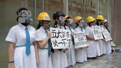 Students wearing gas masks and helmets hold a banner which reads "Five major demands are indispensable.", at St. Francis' Canossian College. AP