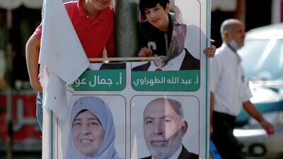 Youths pose for a picture through a tear in a campaign poster of candidates for the upcoming Jordanian parliamentary elections line a street in the capital Amman. AFP