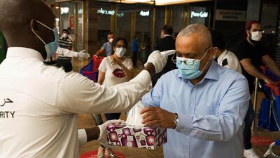 A security guard checks a customer's temperature and offers disposable gloves at Carrefour in Mall of the Emirates. Jon Gambrell / AP