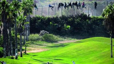 A golfer hits a tee shot as African migrants sit atop a border fence during an attempt to cross into Spanish territory, between Morocco and Spain’s north African enclave of Melilla, in this October 22 file photo. Jose Palazon / Reuters