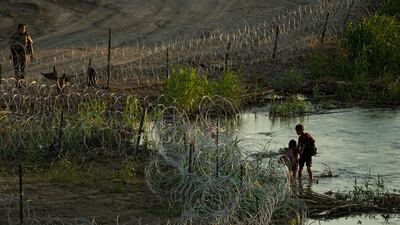 A Texas state trooper watches as young migrants walk along along the banks of the Rio Grande as they try to enter the US from Mexico. AP