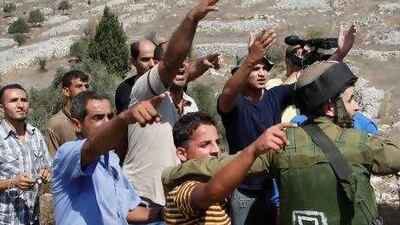 An Israeli soldier separates Palestinian farmers from Israeli settlers in the West Bank village of Burin yesterday.