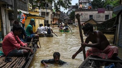 A man sitting on a boat helps a man to navigate his way through floodwaters in Ghatal, Paschim Medinipur district, India.