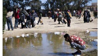 A migrant worker from Bangladesh washes off in a puddle at the Ras Ajdir border checkpoint yesterday in Libya.