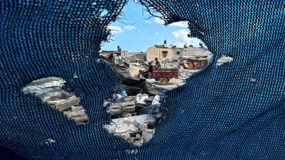 Palestinians, seen through a tear in a tent, ride a motorised vehicle through the rubble in Khan Younis. Reuters