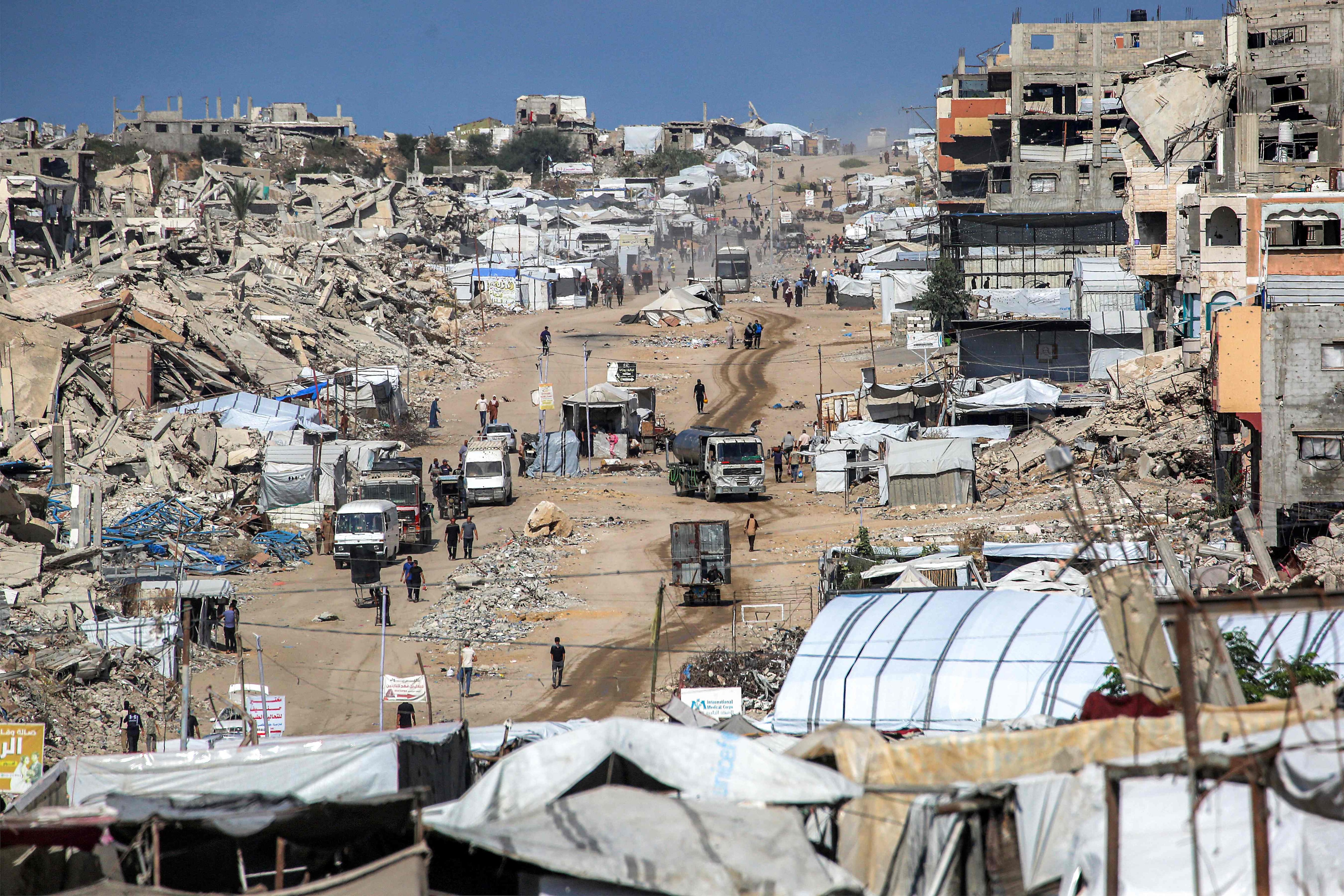 Vehicles drive past collapsed buildings and temporary shelters in the Jabalia camp in the northern Gaza. AFP