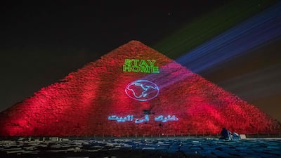 A man takes pictures in front of the Great pyramid of Kheops where a laser projection writes "Stay home" on March 30, 2020. AFP