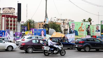 An Iraqi policeman on a motorcycle rides past electoral banners in Baghdad on April 28, 2018, a day after many were damaged by a storm. Sabah Arar / AFP