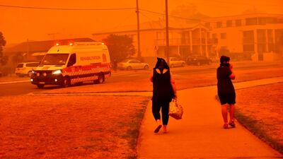 A Fire and Rescue NSW Rehabilitation vehicle drives past people walking along a road shrouded in smoke in Batemans Bay, New South Wales, Australia. Bloomberg