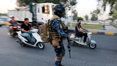 Men ride motorbikes past a member of Iraqi federal police in a street in Baghdad, Iraq. REUTERS