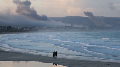 People walk on a beach as smoke billows over southern Lebanon following Israeli strikes, as seen from Tyre, southern Lebanon. Reuters
