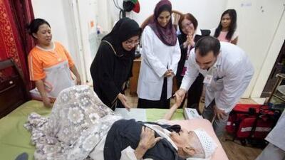 Family and carers work together to ensure Sayed Al Hashemi, centre, is well taken care of at his home in Dubai. Above, Sayed’s daughter Maryam, in the abaya, speaks with her father as he shakes hands with his physiotherapist, Iftikhar Shalla, last week. Jaime Puebla / The National