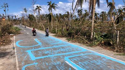 Motorists drive past signs asking for help painted on a road in General Luna town. AFP