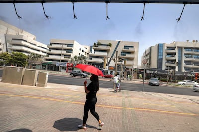 A woman walks with a parasol umbrella underneath sprinklers releasing water vapour in Dubai. Photo AFP