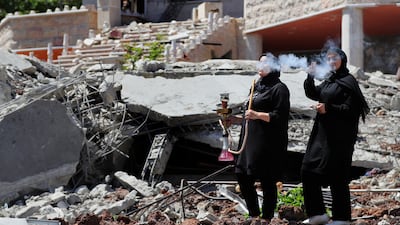 A Lebanese woman smokes a shisha as another woman flashes a victory sign, while standing on the rubble of a destroyed house that was hit by an Israeli air strike, in Aita al Shaab, a Lebanese border village with Israel, south Lebanon. AP