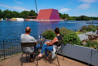 A couple watch as workers build 'The Mastaba', an outdoor work made up of over 7000 stacked barrels by Bulgarian artist Christo Vladimirov Javachef on the Serpentine lake in Hyde Park in London on June 11, 2018. / AFP / Niklas HALLEN