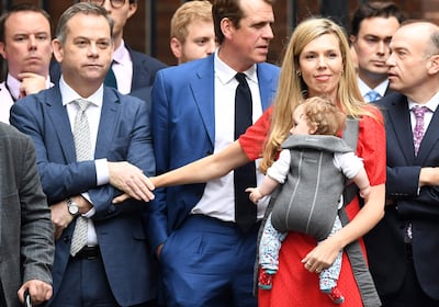 Carrie Johnson (2ndR), wife of Britain's Prime Minister Boris Johnson, carrying their daughter Romy holds onto Britain's Minister without Portfolio Nigel Adams as the premier delivers a statement in front of 10 Downing Street in central London on July 7, 2022. - Johnson quit as Conservative party leader, after three tumultuous years in charge marked by Brexit, Covid and mounting scandals. (Photo by Daniel LEAL / AFP)