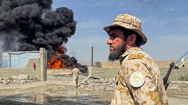 A Taliban security personnel stands guard as smoke rises following Pakistani air strikes that hit oil depots near the Kandahar airport in the Daman district of Kandahar province. AFP