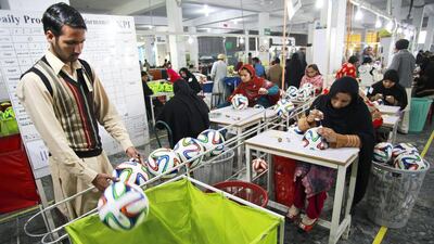 An employee places an Adidas AG "Brazuca Replica Glider" football into a trolley on the production line at the Forward Sports factory in Sialkot, Punjab. Asad Zaidi / Bloomberg