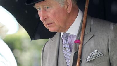 Prince Charles, Prince of Wales, shelters from the rain under an umbrella. Getty Images