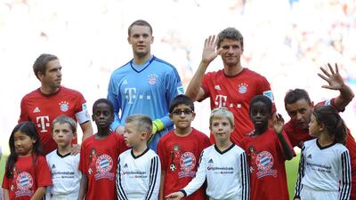 Left to right: Bayern Munich's defender Philipp Lahm, Manuel Neuer and Thomas Mueller stand with migrant children (in red) prior to the German first division Bundesliga football match FC Bayern Munich v FC Augsburg, in Munich, on September 12, 2015. Andandreas Gebert / AFP