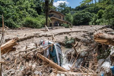 A car lies in mud as people rest in the shade of a house that is partially submerged as they search for missing relatives following a landslide. Getty Images