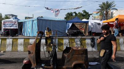 An anti-government protester walks past a burnt tuk-tuk in Baghdad's Tahrir Square, Iraq. AP