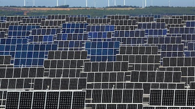 Photovoltaic power panels stand at Abaste's El Bonillo solar plant while wind turbines spin at a wind farm on the background in Spain. Pablo Blazquez Dominguez / Getty Images