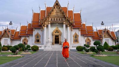 A Buddhist monk goes to collect alms in front of a temple in Bangkok. AFP