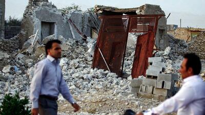 Iranians walk past the ruins of a destroyed house in the town of Shonbeh, southeast of Bushehr. AFP PHOTO / MOHAMMAD FATEMI