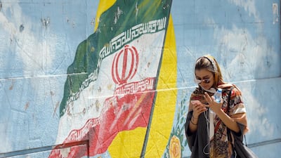 An Iranian girl walks next to a wall painting of Iran's national flag while using her cellphone in a street, in Tehran, Iran, 28 April 2018. Abedin Taherkenareh / EPA