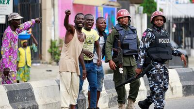 Men gesture as they stand near police officers along a street in Ikeja, as Nigeria's Lagos state remains under curfew. Reuters