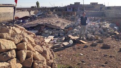 Mohammed Khader Suleiman, 53, stands amid the ruins of his two houses adjacent to a school in Mosul Dam. A red flag, marking a possible IED, stands in the foreground. Jonathan Krohn for The National