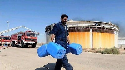 A man carries containers past a smoking oil tank in the eastern oil town of Brega. EPA