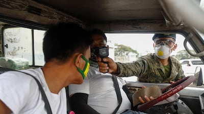 A Philippine Army soldier uses a thermal scanner to check body temperature of two men in a vehicle entering a quarantine border of Quezon City, Metro Manila. EPA