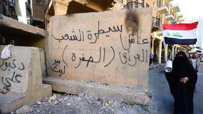 A female protester carrying the Iraqi national flag walks past a concrete block with a slogan reading in Arabic: 'The checkpoint of the people, long live Iraq' written on it, during a protest at the Tahrir square in central Baghdad. EPA