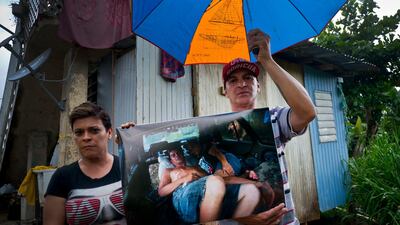 Blanca Rivera and Eduard Rodriguez pose with a printed photo of them that was taken on September 30, 2017 of them sleeping in their car. The couple said authorities rejected their request for financial help to rebuild, so they sold their car to build a room next to his mother's house.