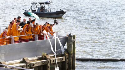July 16, 2011: The Dalai Lama, third from left in a baseball cap, pours mandala sand mixed with river water into the Anacostia River as part of a blessing ceremony in Washington. AP Photo/Jacquelyn Martin