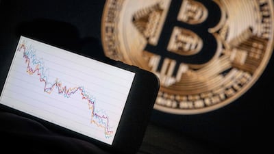 This illustration photograph shows a phone with a downward trend in the stock market in front of a screen displaying a Bitcoin logo, in Mulhouse on December 5, 2025. (Photo by SEBASTIEN BOZON / AFP)