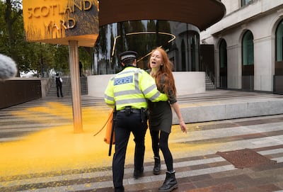 A Just Stop Oil protester is led away by police after spray painting a sign outside New Scotland Yard in London. PA.