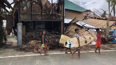 Young surfers pass houses destroyed by super Typhoon Rai on their way to the beach in General Luna town, Siargao island. AP