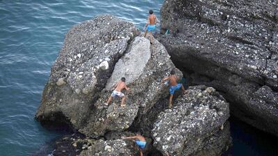 Boys climb a rock before jumping into the Mediterranean Sea on El Salon beach near Malaga (REUTERS/Jon Nazca)